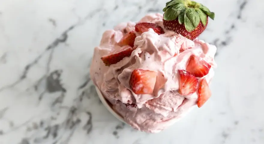 Un délice rose et crémeux : un sorbet fraise garni de morceaux de fruits frais et d'une fraise entière sur un fond marbré.