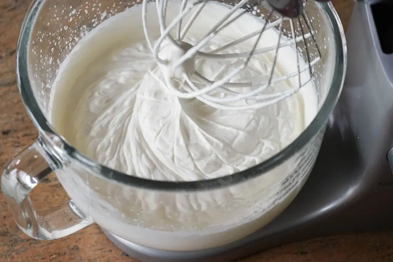 La cr&egrave;me fouett&eacute;e est presque pr&ecirc;te dans le bol en verre. Le batteur est en train de la monter, montrant comment faire de la chantilly parfaite.