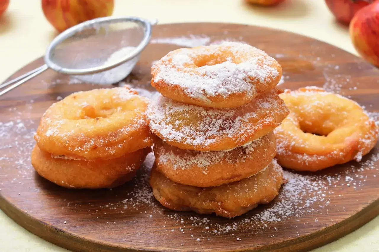 Pile de beignets aux pommes saupoudr&eacute;s de sucre glace, pr&ecirc;ts &agrave; &ecirc;tre d&eacute;gust&eacute;s.
