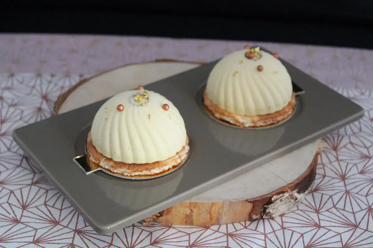 Deux d&ocirc;mes de dessert fruit&eacute;s, orn&eacute;s de perles cuivr&eacute;es et de feuilles d'or, sur un plateau gris.