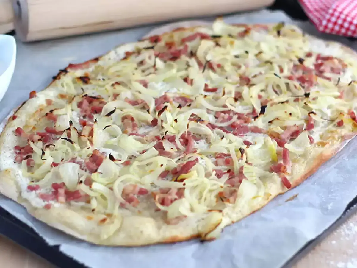 Flammekueche pr&ecirc;te &agrave; &ecirc;tre d&eacute;gust&eacute;e, avec sa garniture g&eacute;n&eacute;reuse d'oignons et de lardons. Une recette simple et savoureuse.