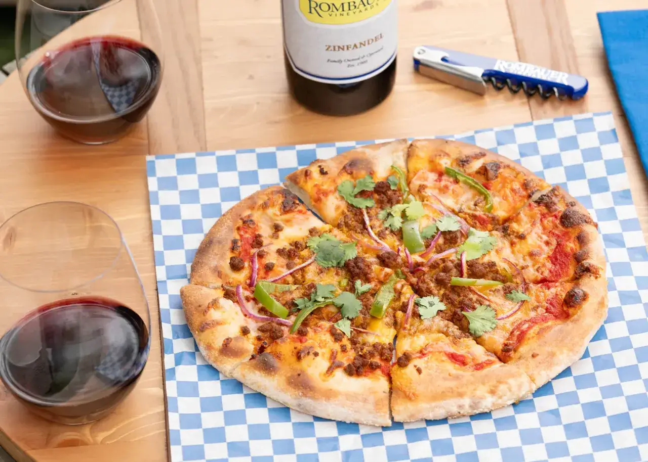 Une pizza chorizo app&eacute;tissante, garnie de poivrons verts et d'oignons rouges, est pr&ecirc;te &agrave; &ecirc;tre d&eacute;gust&eacute;e avec un verre de vin rouge.