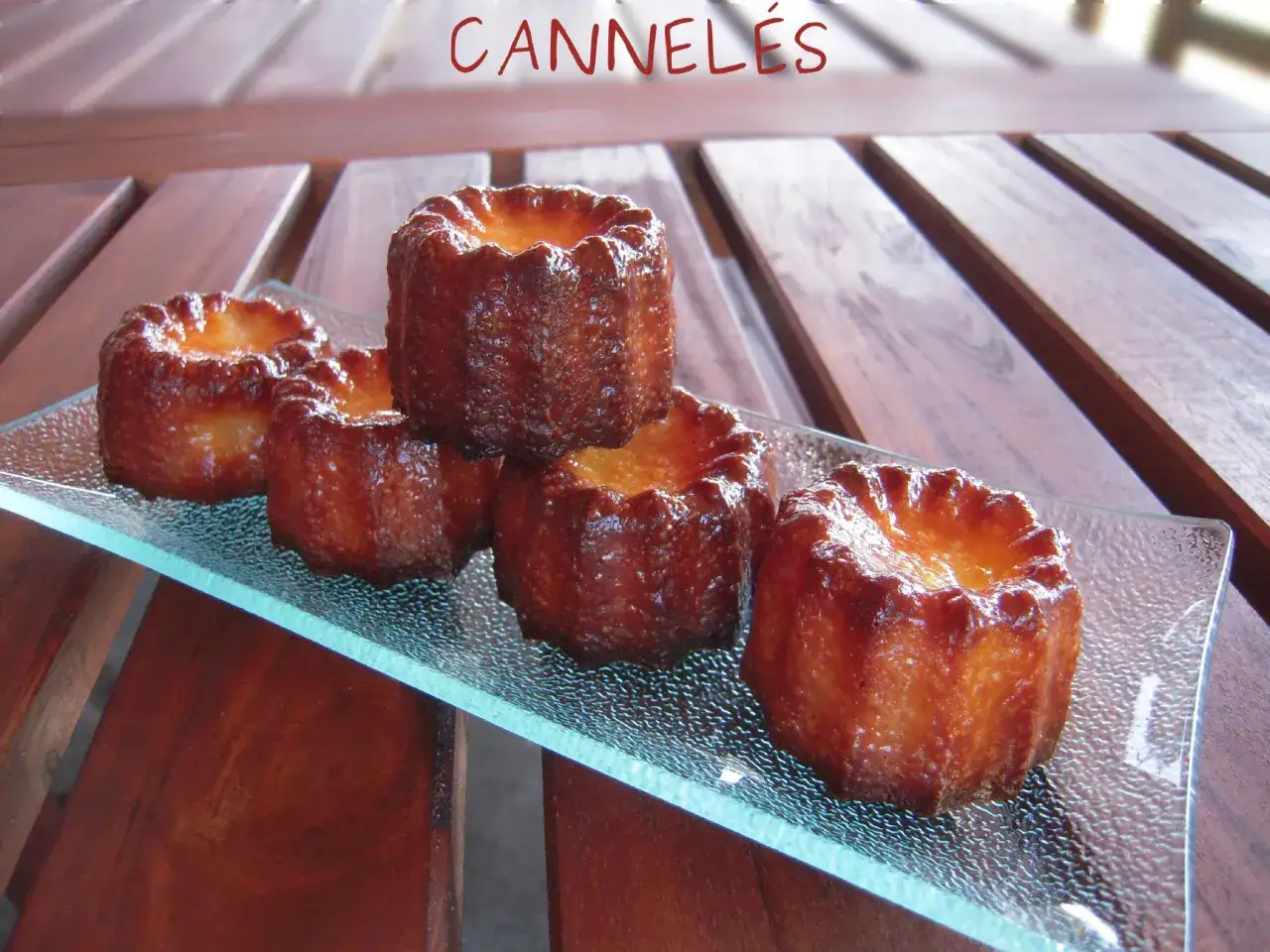 Cinq cannel&eacute;s dor&eacute;s, parfaits pour une recette cannel&eacute;s moule silicone. Ils sont pr&eacute;sent&eacute;s sur un plat en verre textur&eacute;.