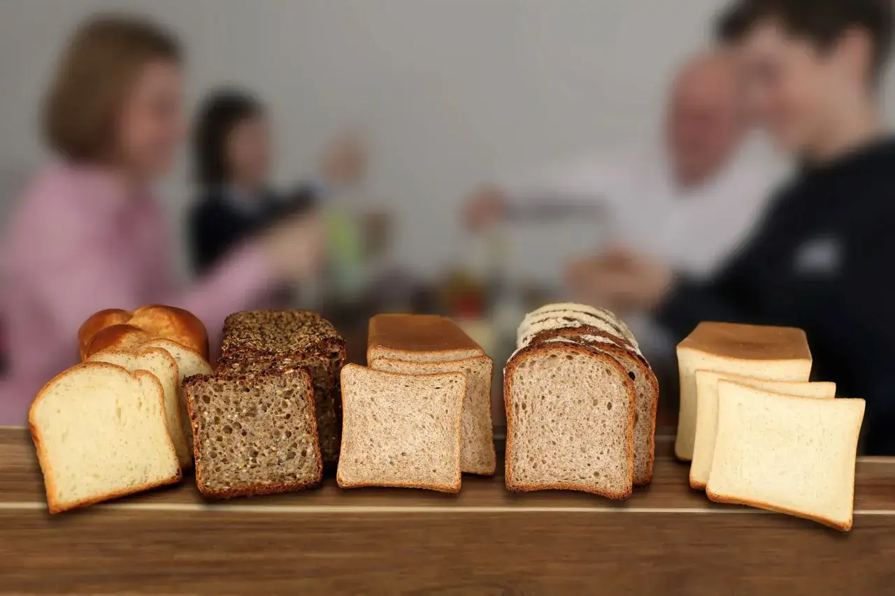 Une vari&eacute;t&eacute; de pains, dont du pain au son, est pr&eacute;sent&eacute;e sur une table en bois. Au fond, une famille est floue.