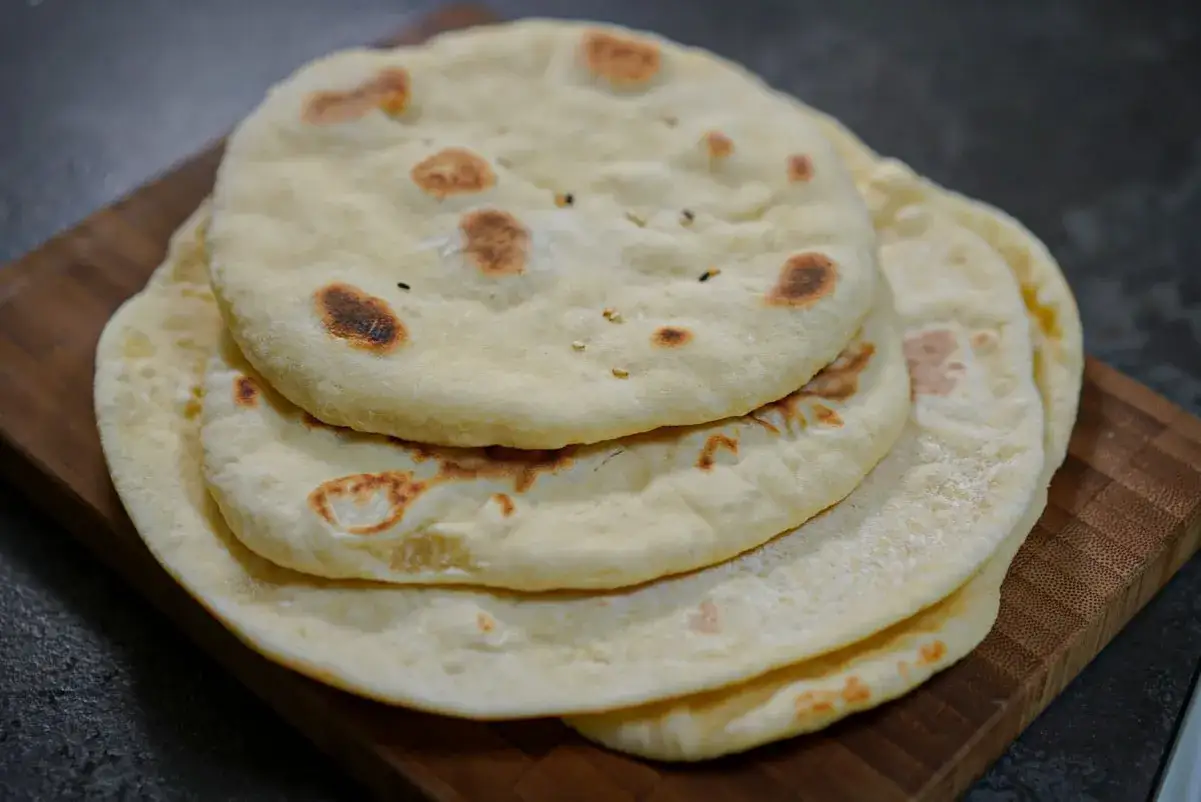 Pile de pains libanais moelleux, l&eacute;g&egrave;rement dor&eacute;s par la cuisson, sur une planche en bois.