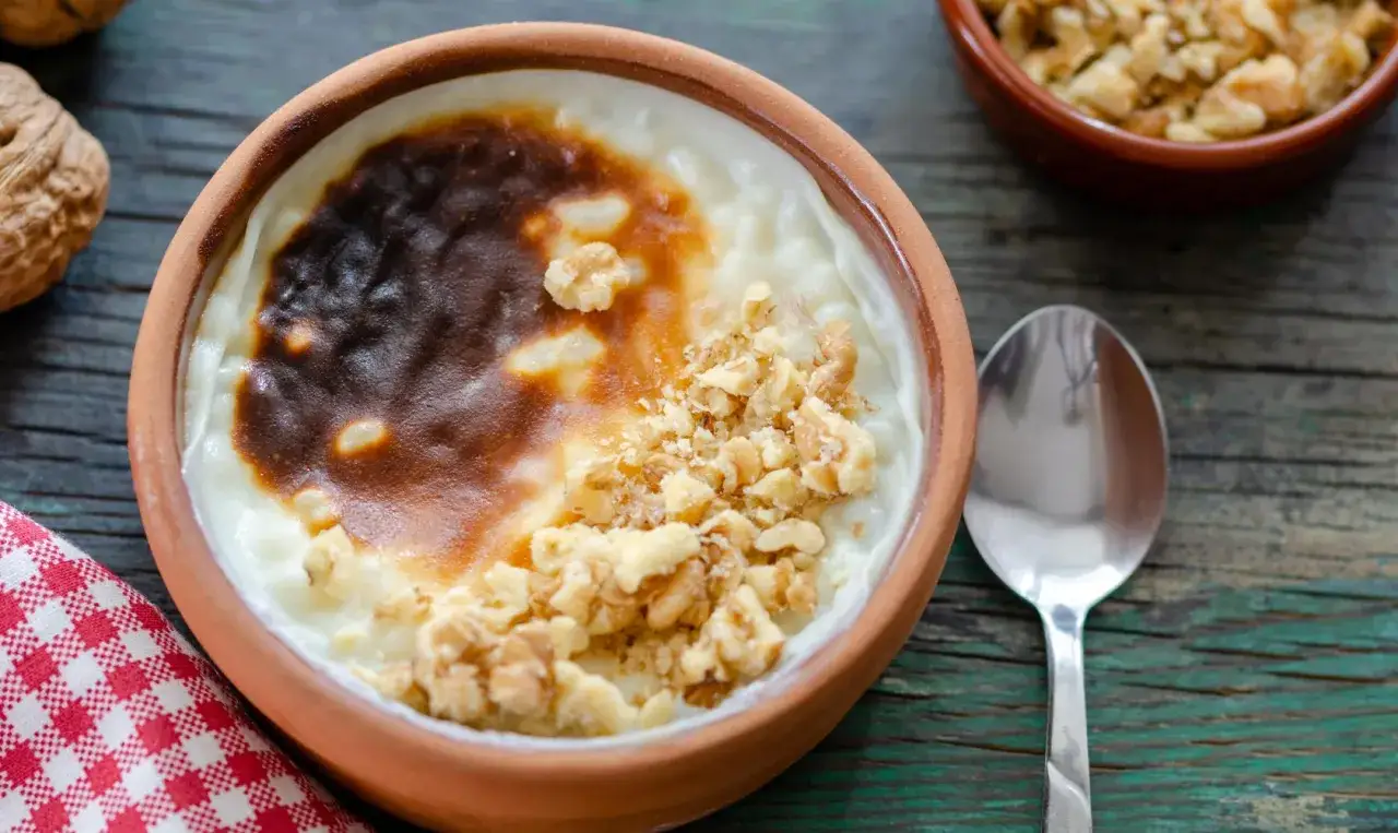 Un d&eacute;licieux riz au lait au four, gratin&eacute; et parsem&eacute; de noix concass&eacute;es, servi dans un bol en terre cuite.