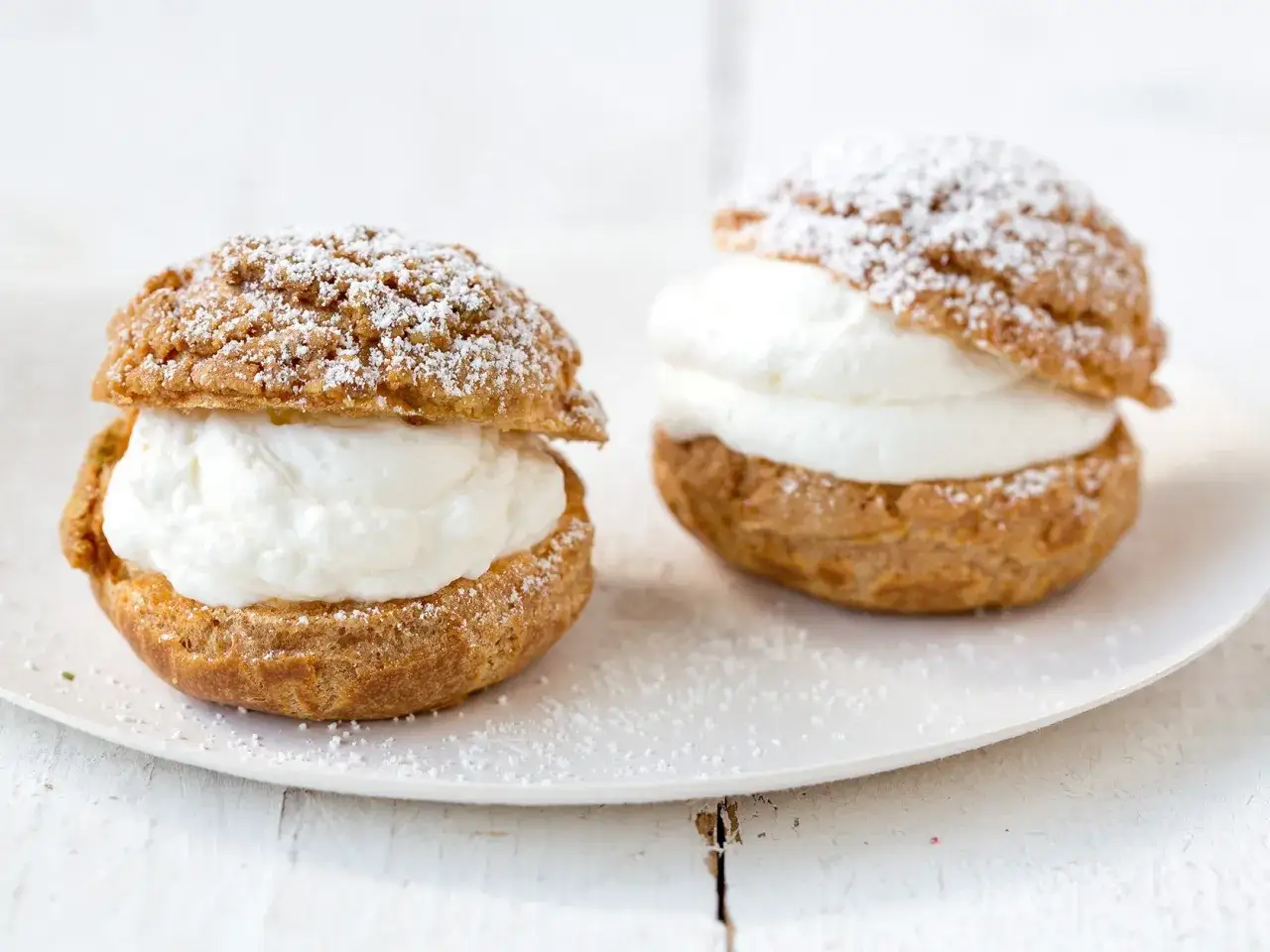 Deux choux &agrave; la cr&egrave;me g&eacute;n&eacute;reusement garnis de cr&egrave;me fouett&eacute;e, saupoudr&eacute;s de sucre glace sur une assiette blanche.