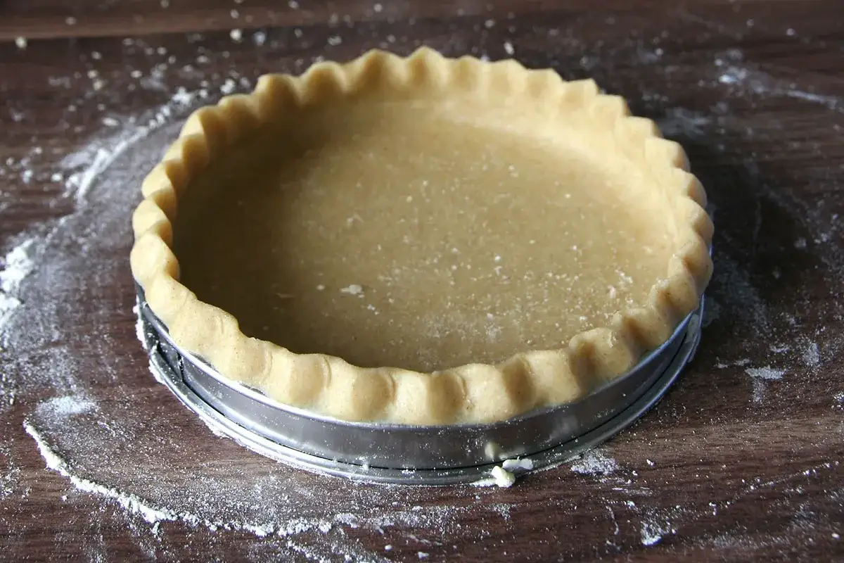 Une p&acirc;te &agrave; tarte maison, pr&ecirc;te &agrave; &ecirc;tre garnie, repose dans un moule &agrave; tarte sur un fond en bois parsem&eacute; de farine.