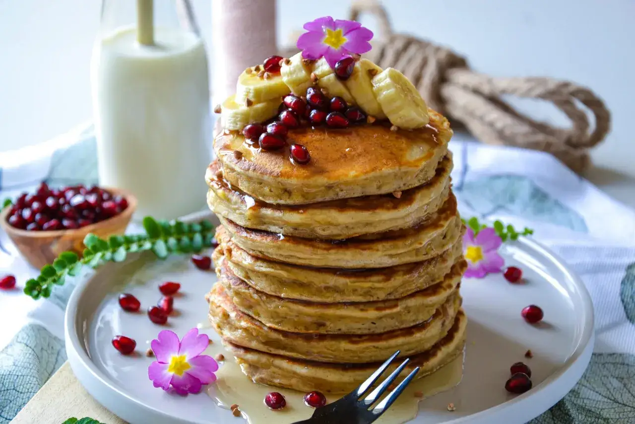 Pile de pancake banane, garnie de fruits rouges, de rondelles de banane et de fleurs roses. Un d&eacute;lice pour le petit-d&eacute;jeuner.