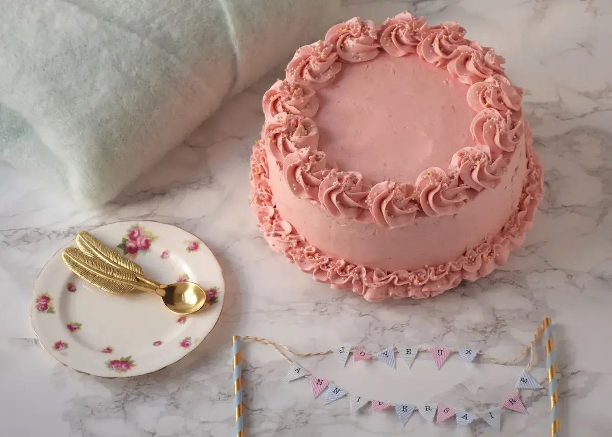 G&acirc;teau rose pastel, d&eacute;cor&eacute; de volutes et de perles. Une petite assiette avec une cuill&egrave;re dor&eacute;e en forme de plume et une guirlande 