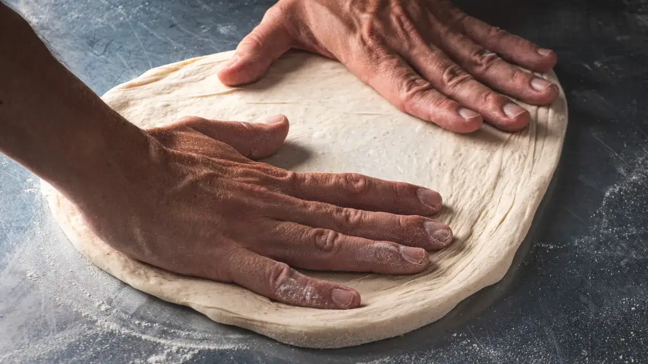 Mains travaillant la pâte pour une pizza maison. La farine est saupoudrée sur la surface de travail.