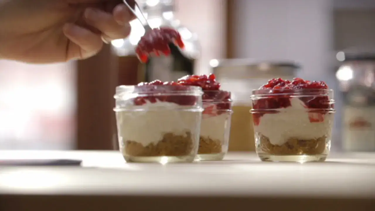 Une main ajoute une garniture rouge sur un cheesecake sans cuisson en pot. Délicieux dessert individuel.