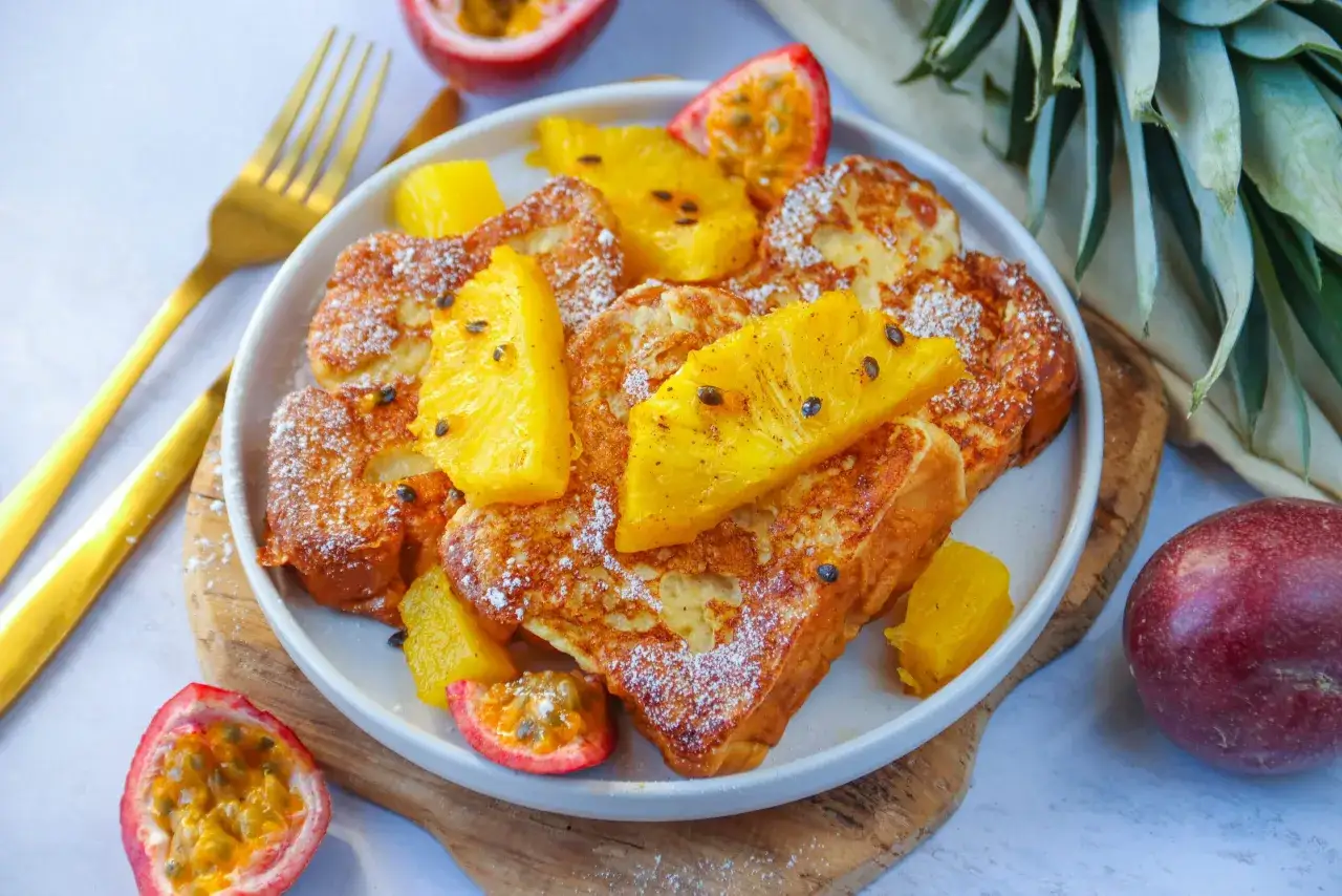 Une assiette de brioche perdue dor&eacute;e, garnie de fruits de la passion et d'ananas frais, saupoudr&eacute;e de sucre glace.