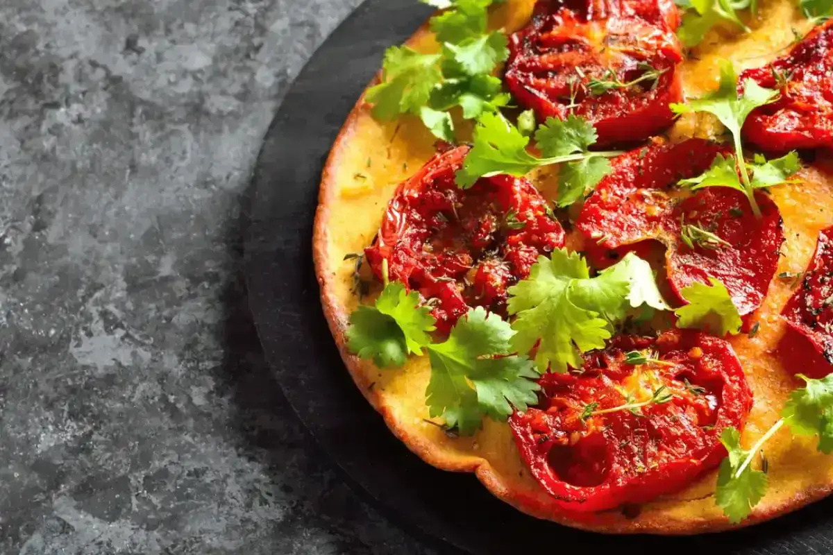 Une socca dor&eacute;e garnie de tomates r&ocirc;ties et de coriandre fra&icirc;che. Une recette simple et savoureuse pour un ap&eacute;ritif m&eacute;diterran&eacute;en.