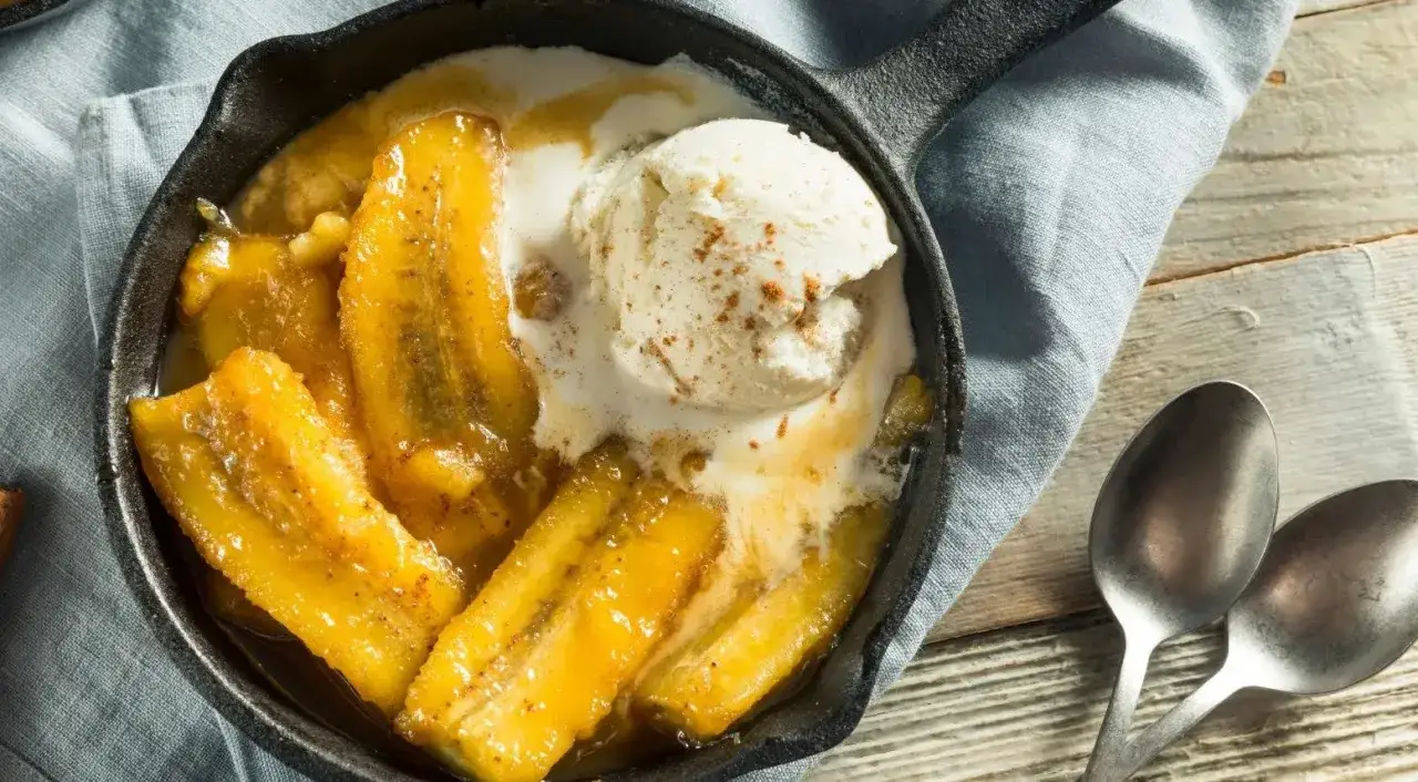 Banane flambée servie dans une poêle en fonte, nappée de glace à la vanille et saupoudrée de cannelle. Un délice gourmand.