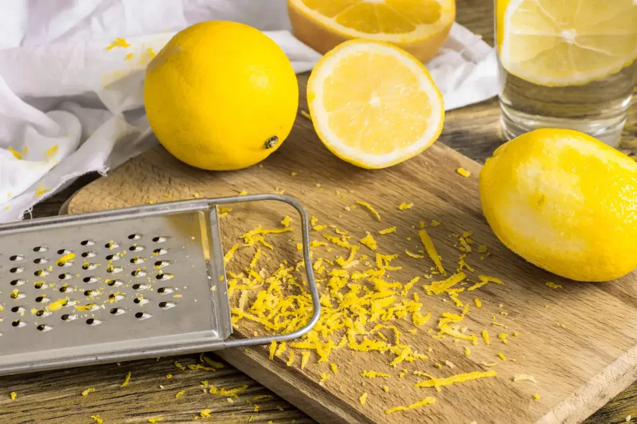 Un r&acirc;pe et des citrons frais sur une planche en bois, avec du zeste de citron &eacute;parpill&eacute;.