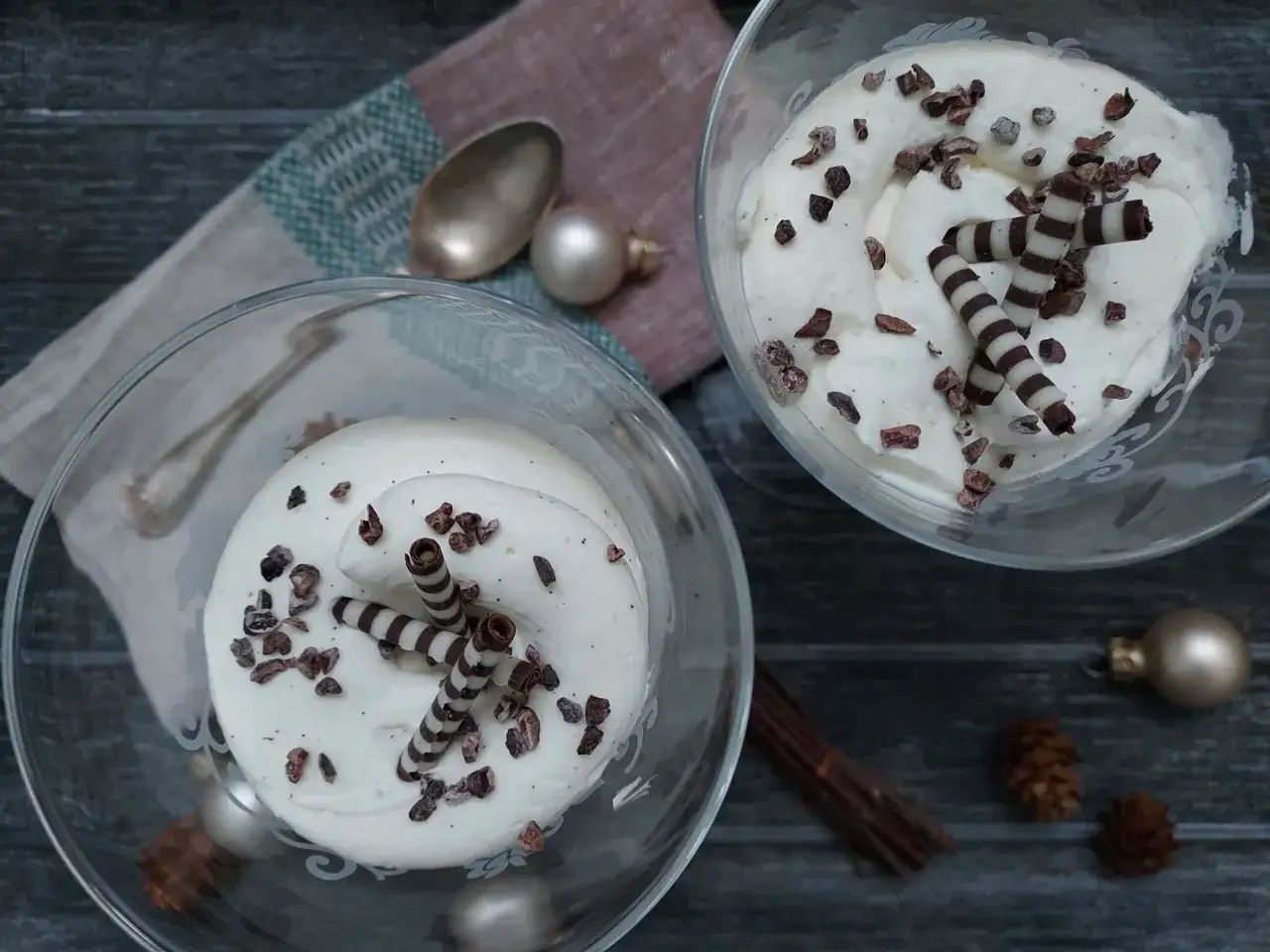 Deux coupes de chantilly chocolat blanc, parsem&eacute;es de cacao et d&eacute;cor&eacute;es de rouleaux de chocolat. Une ambiance festive avec des boules de No&euml;l et des pommes de pin.