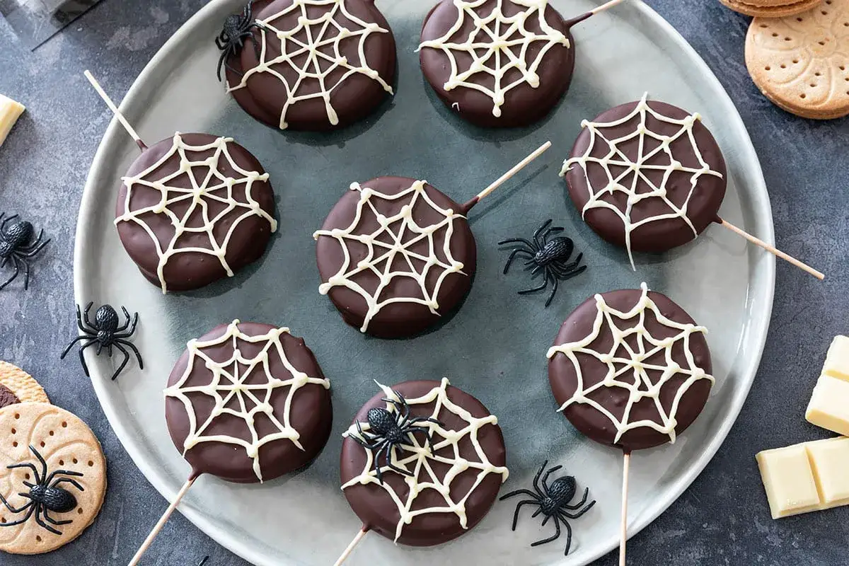 D&eacute;licieux dessert Halloween : des biscuits enrob&eacute;s de chocolat noir, d&eacute;cor&eacute;s de toiles d'araign&eacute;es blanches et orn&eacute;s d'araign&eacute;es en plastique.