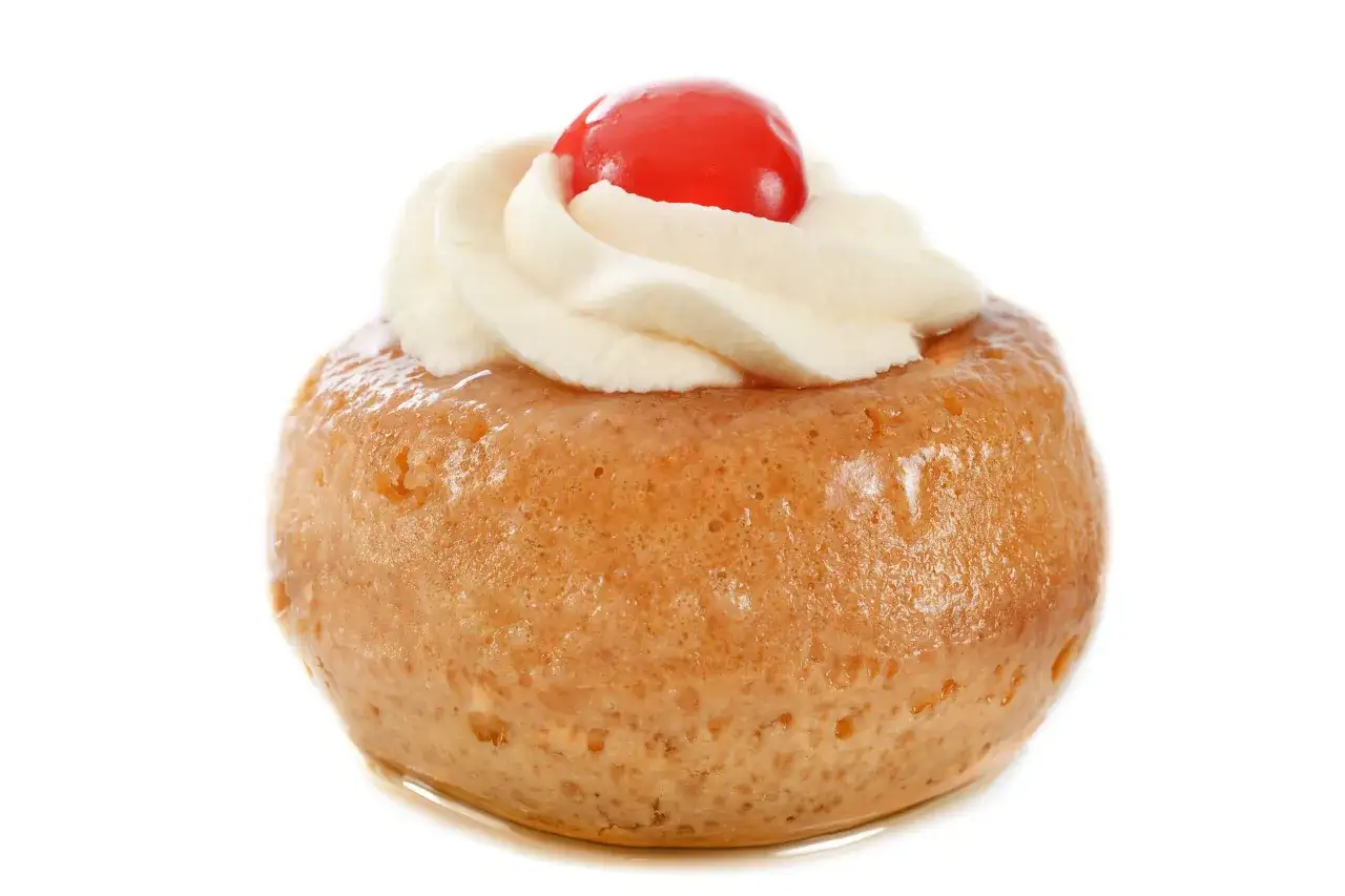 Un d&eacute;licieux baba au rhum, moelleux et imbib&eacute;, surmont&eacute; de cr&egrave;me fouett&eacute;e et d'une cerise rouge.