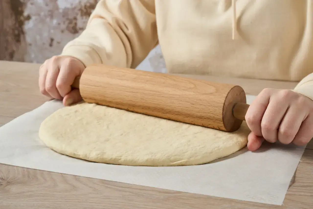 Mains travaillant avec un rouleau à pâtisserie sur une pâte sablée étalée sur du papier sulfurisé.