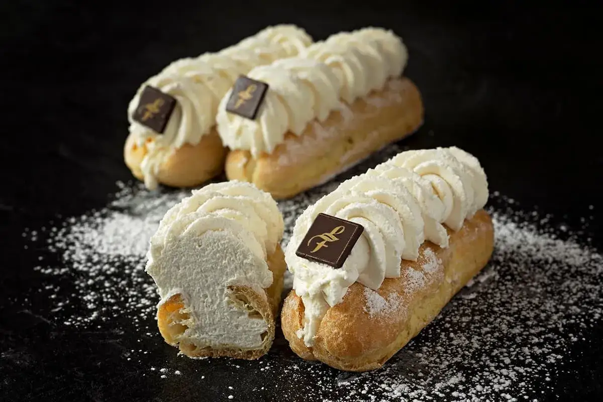 Trois &eacute;clairs chantilly g&eacute;n&eacute;reusement garnis de cr&egrave;me fouett&eacute;e, orn&eacute;s d'un carr&eacute; de chocolat, saupoudr&eacute;s de sucre glace.