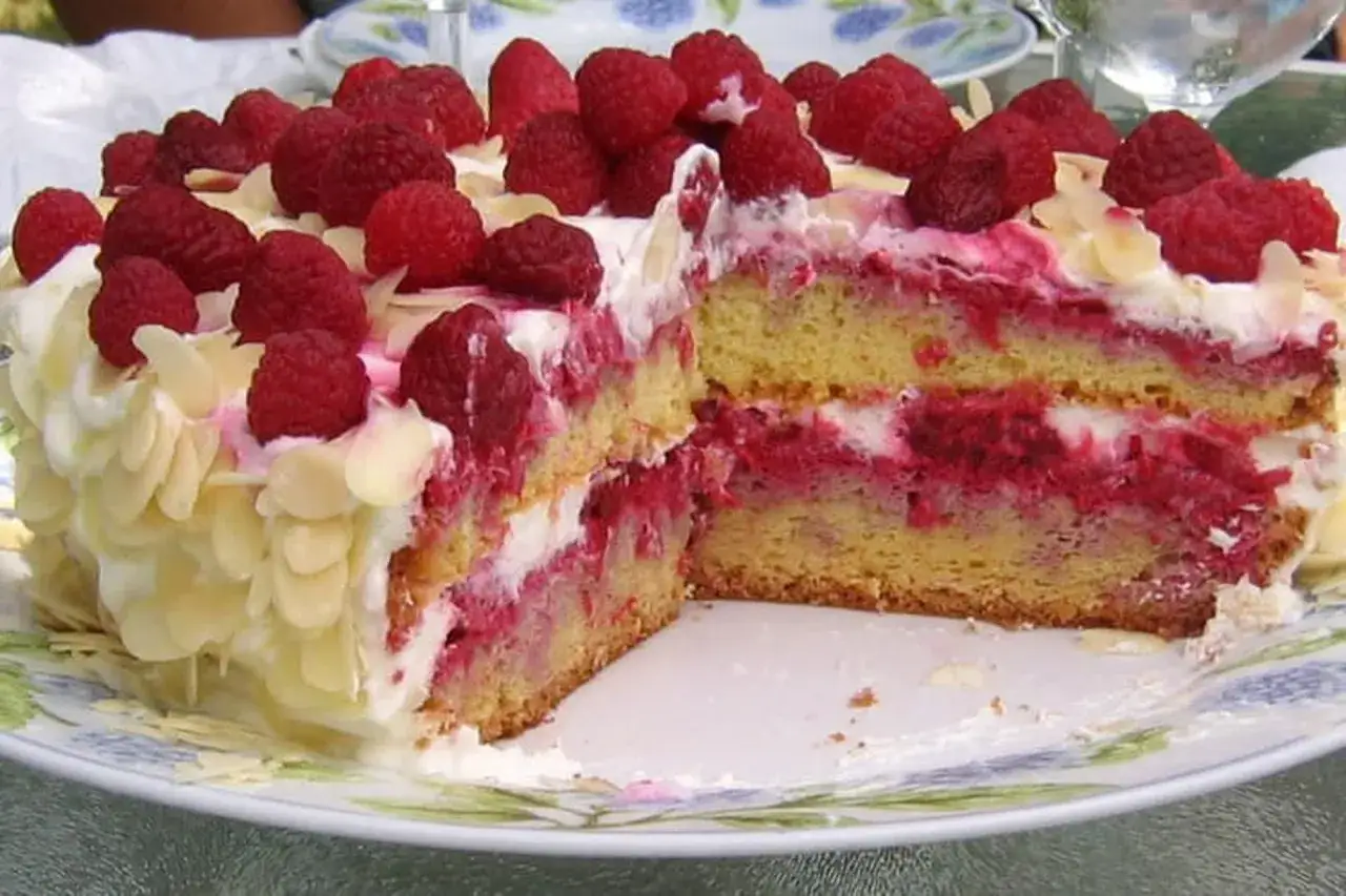 Un délicieux framboisier gateau, garni de framboises fraîches et d'éclats d'amandes, est coupé en deux sur une assiette fleurie.