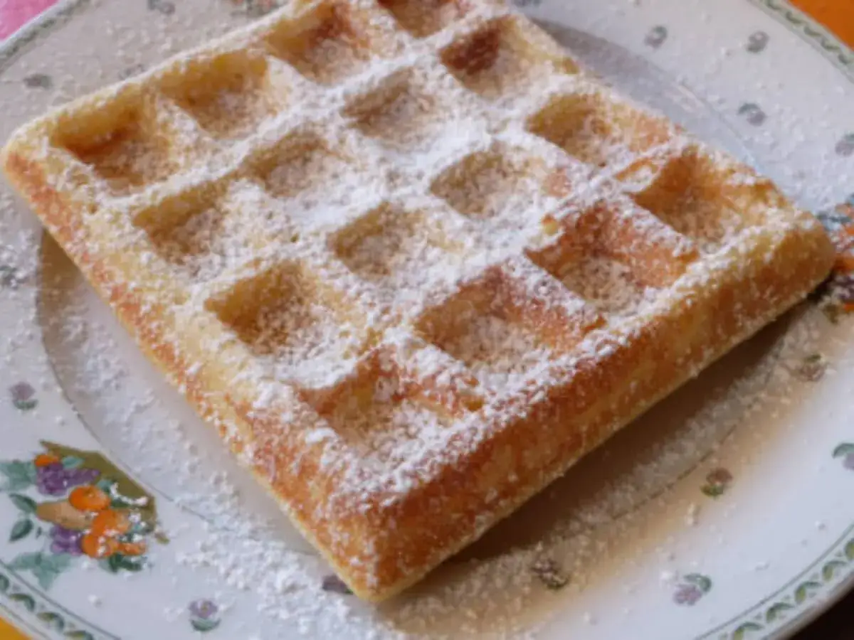 Une gaufre lyonnaise dor&eacute;e, saupoudr&eacute;e de sucre glace, repose sur une assiette d&eacute;cor&eacute;e de fleurs. Un d&eacute;lice simple et gourmand.