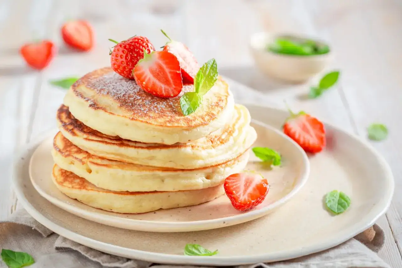 Pile de pancakes moelleux, saupoudr&eacute;s de sucre glace et orn&eacute;s de fraises fra&icirc;ches, comme ceux de Cyril Lignac.