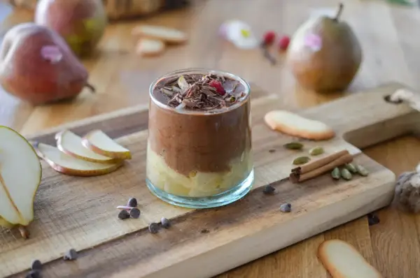 Délicieuse recette mousse poire chocolat, garnie de copeaux de chocolat et d'une framboise. Poires fraîches et épices sur fond de bois.