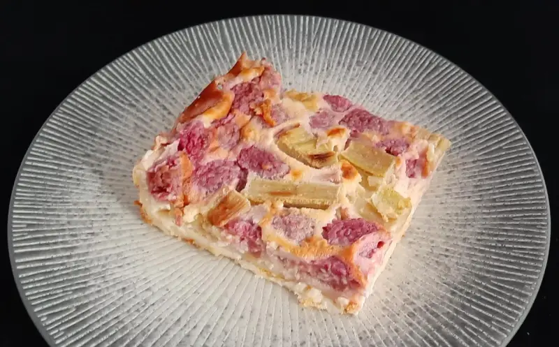 Tranche de clafoutis rhubarbe aux fruits rouges, sur une assiette transparente aux motifs rayonnants.
