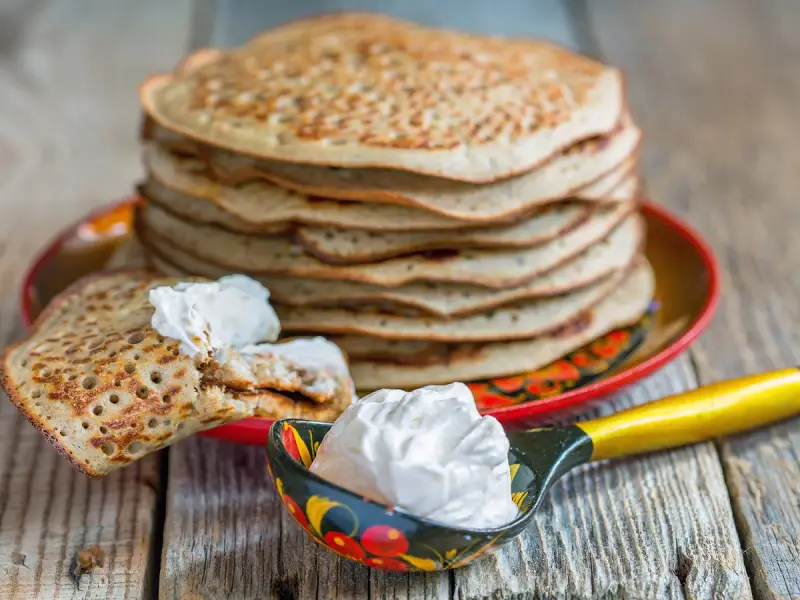 Pile de crêpes épaisses alsaciennes, garnies de crème fraîche. Une cuillère décorée en est aussi remplie.